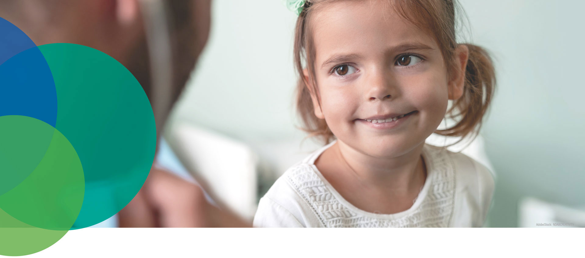 Ein junges Mädchen mit braunen Haaren in Zöpfen und einem weißen Hemd lächelt, während es einen Erwachsenen anschaut, mit sich überlappenden transparenten blauen und grünen Kreisen auf der linken Seite des Bildes.