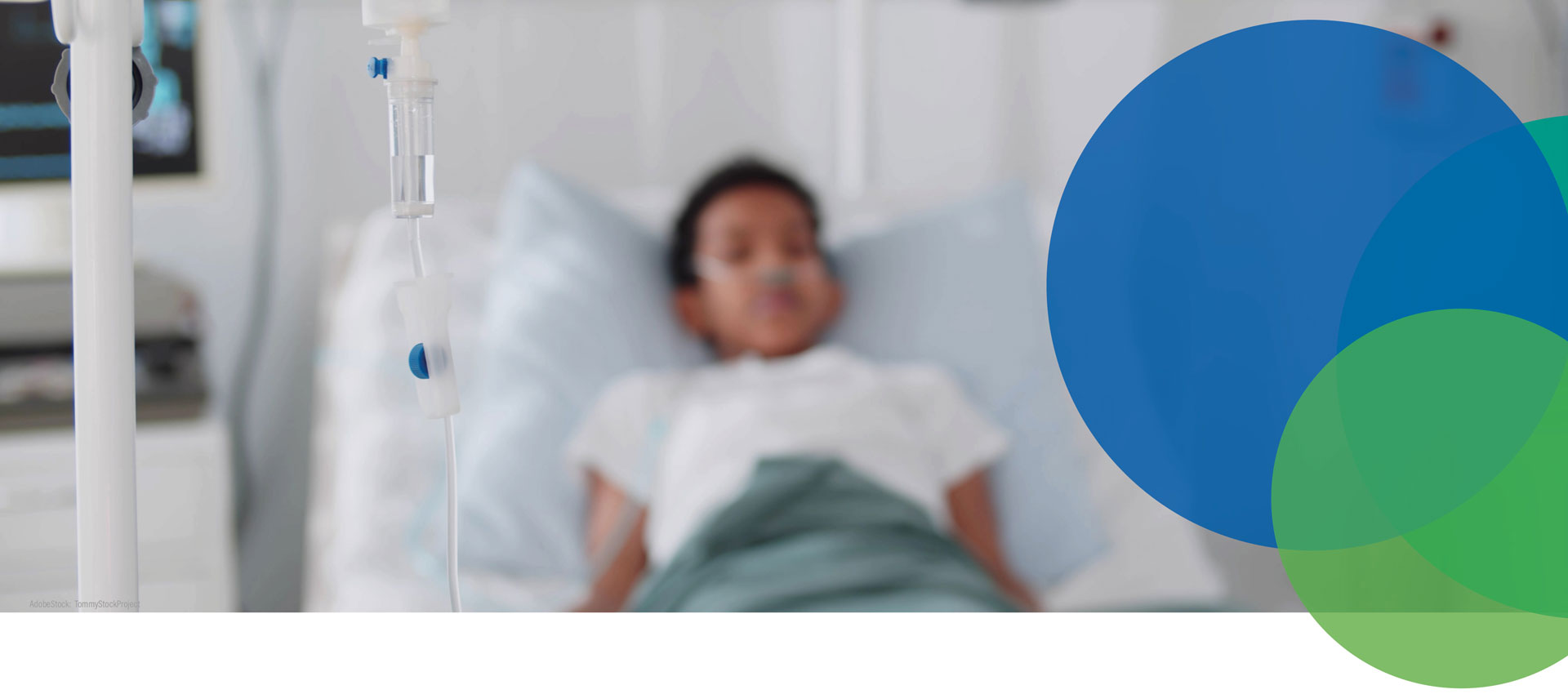 Ein Kind liegt in einem Krankenhausbett mit einem nasalen Sauerstoffschlauch, unscharf im Hintergrund. Im Vordergrund ist ein Infusionstropf scharf abgebildet. Blaue und grüne überlappende Kreise befinden sich auf der rechten Seite des Bildes.