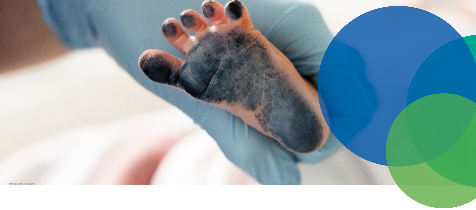 Eine behandschuhte Hand hält einen neugeborenen Babyfuß, der mit schwarzer Tinte bedeckt ist, wahrscheinlich um einen Fußabdruck zu machen. Bunte, sich überlappende Kreise schmücken die rechte Seite des Bildes.