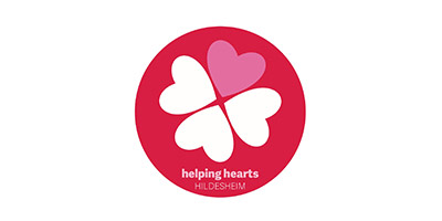 Ein rotes, rundes Logo mit vier Herzformen, die ein Kleeblatt bilden. Drei Herzen sind weiß und eines ist rosa. Darunter steht der Text helping hearts HILDESHEIM.